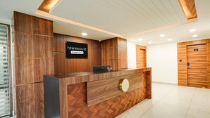A reception desk with a sign reading 'TOWNHOUSE & Company Serviced,' a modern design with wooden paneling, a glass partition, and a digital screen. - Deluxe Onyx Hotel (Bengaluru)