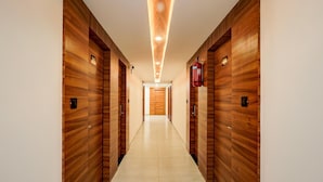 A hallway with wooden paneling, a tiled floor, and a fire extinguisher mounted on the wall. - Deluxe Onyx Hotel (Bengaluru)