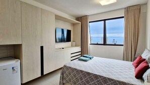 Ein Hotelzimmer mit Bett, Fernseher, Minikühlschrank und einem Fenster mit Blick auf die Stadt.