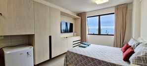 Ein Hotelzimmer mit Bett, Fernseher, Minikühlschrank und einem Fenster mit Blick auf die Stadt.