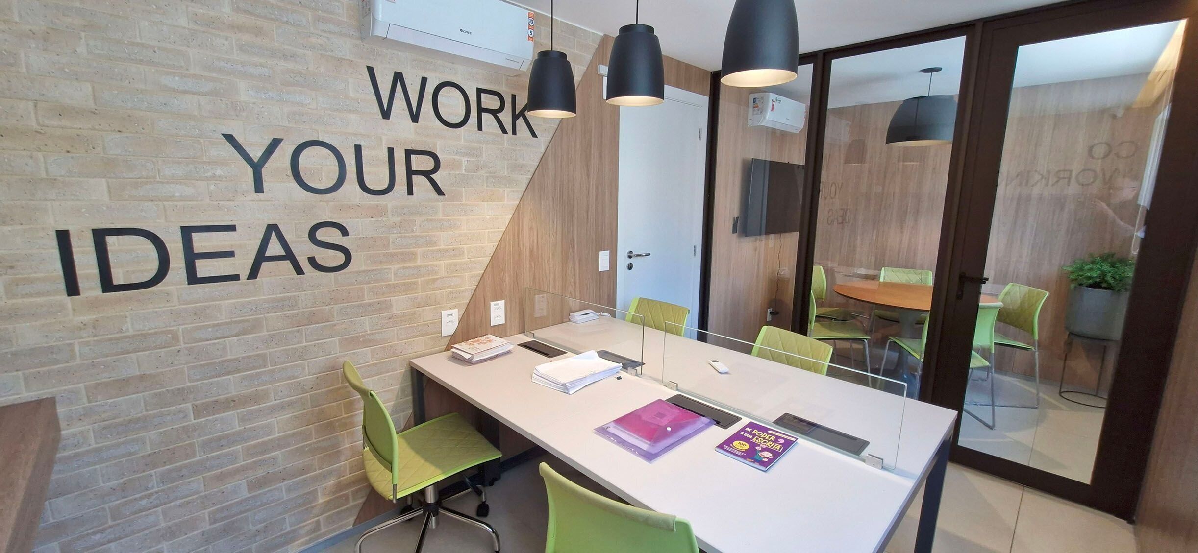 A modern office space with a long table, green chairs, and a wall with motivational text.