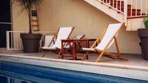 Un área junto a la piscina con sillas de descanso, una planta en maceta y una escalera.