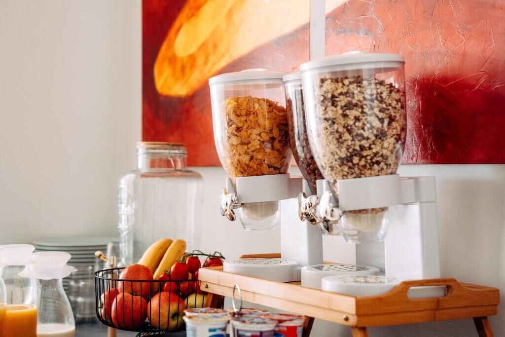 A breakfast bar with cereal dispensers, a fruit basket, and a coffee machine.