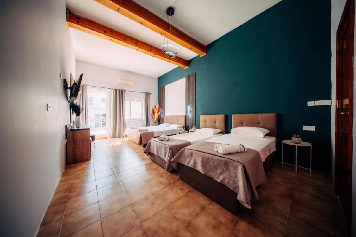 A hotel room with two beds, a wooden ceiling, a large window, and a small side table.