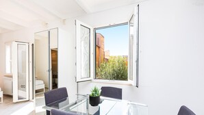 Ein modernes Zimmer mit einem Glastisch, vier Stühlen, einer Topfpflanze und Blick auf Gebäude und Bäume.