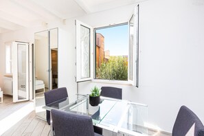 A modern room with a glass table, four chairs, a potted plant, and a view of buildings and trees outside. - Monti Terrace Apartment with stunning views (Rome)