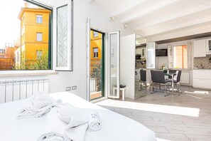 A modern hotel room with a bed, a view of the city, a balcony, and a kitchen area. - Monti Terrace Apartment with stunning views (Rome)