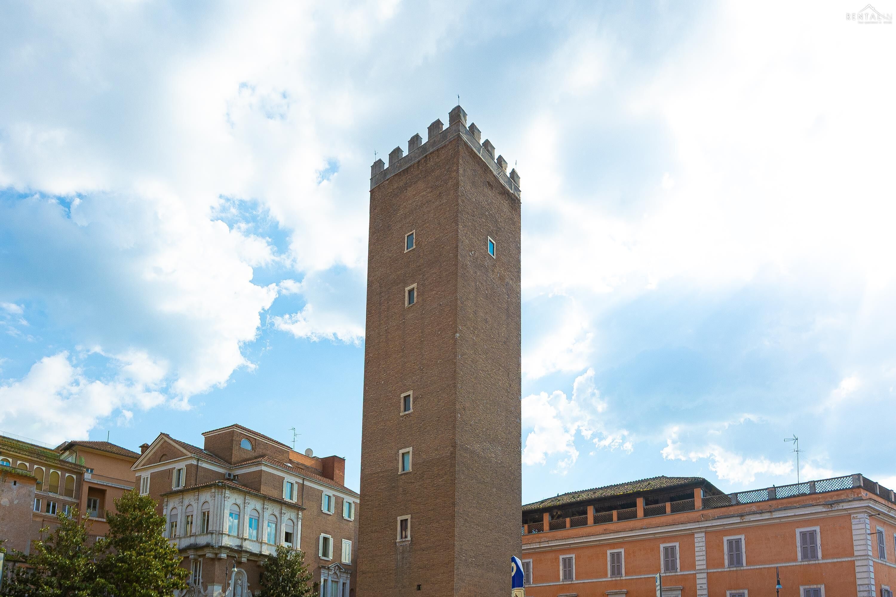 Una alta torre de ladrillo con almenas, rodeada de edificios históricos de arquitectura clásica.
