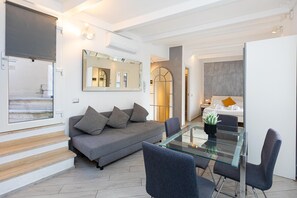 A modern living room with a glass dining table, grey sofa, and a large mirror. - Monti Terrace Apartment with stunning views (Rome)