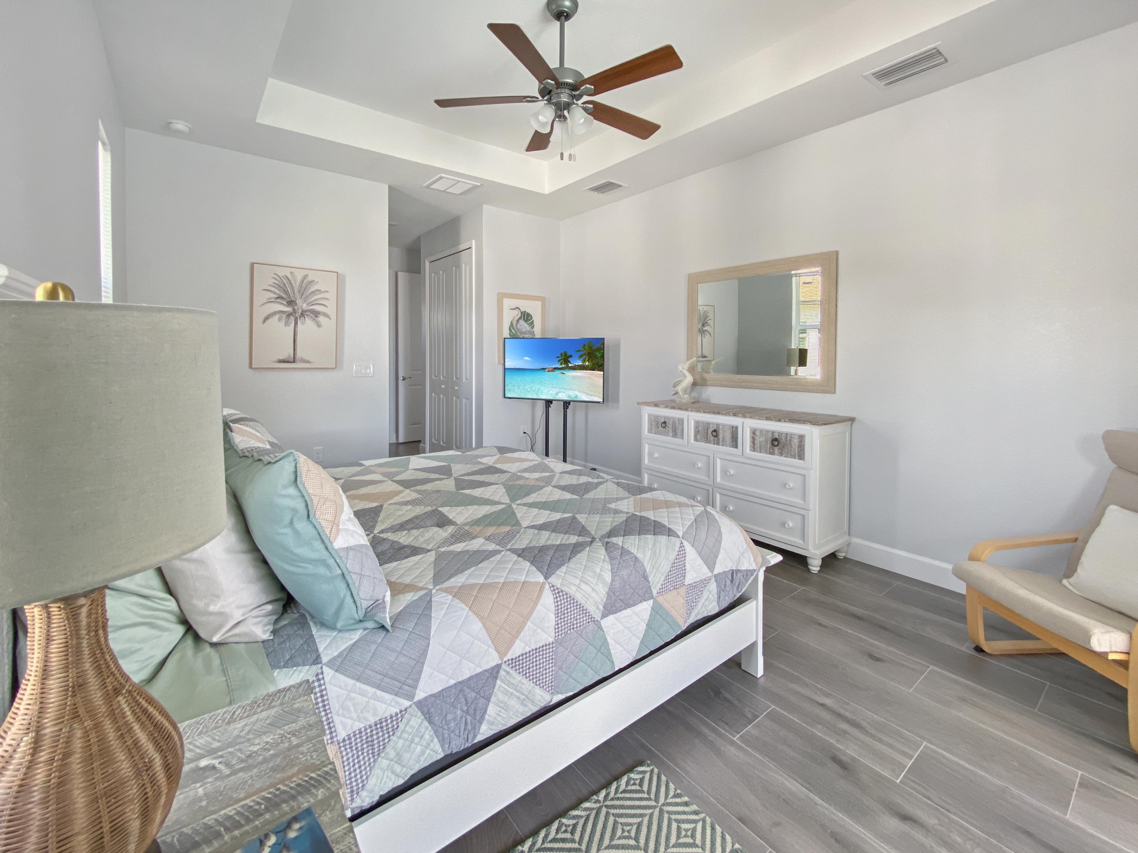 A bedroom with a bed, a ceiling fan, a television, a dresser, and a chair.