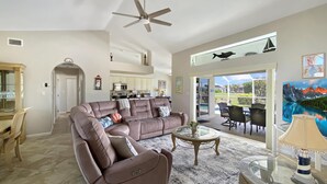 Uma sala de estar ampla com um grande sofá de couro, uma mesa de centro de vidro e uma área de jantar com cadeiras.