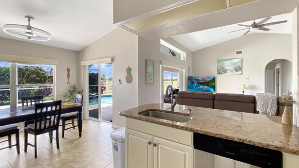 Cozinha moderna com ilha central, área de jantar com mesa e cadeiras, e vista para uma piscina por grandes janelas.