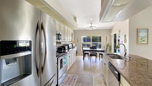 Cozinha moderna com eletrodomésticos de aço inoxidável, área de refeições com mesa e cadeiras, e vista pela janela.