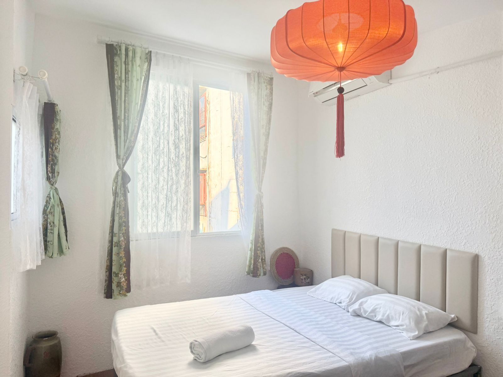 Une chambre d’hôtel avec un lit, des rideaux, une lanterne suspendue et une fenêtre.