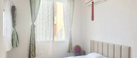 A hotel room with a bed, curtains, a hanging lantern, and a window.