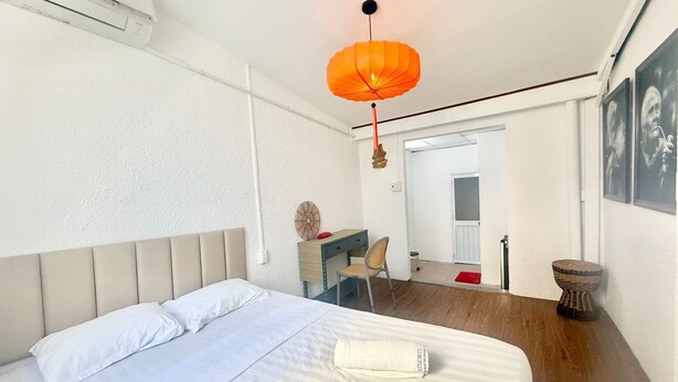 A bedroom with a bed, a desk, a chair, a hanging lamp, and a door leading to another room. - Cherry Blossom Boutique Hotel (Ho Chi Minh City)