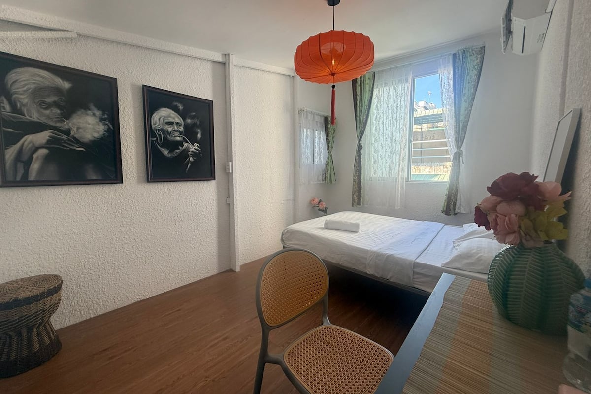 A room with a bed, a chair, a table, and two framed pictures on the wall.
