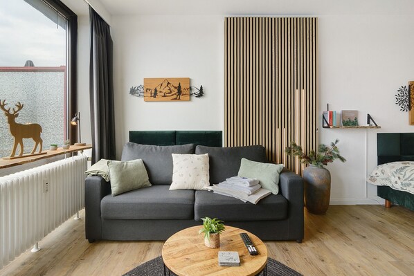 Ein modernes Wohnzimmer mit grauem Sofa, einem Holztisch und Blick ins Freie.