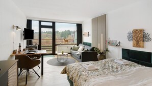 A modern hotel room with a large bed, a desk with a chair, a sofa, a TV, and a view of the outdoors. - Apartment 'Panoramablick Hahnenk' with Sea View, Wi-Fi and Air Conditioning (Goslar)