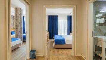 Une chambre d’hôtel avec un plancher en bois, un lit recouvert d’une courtepointe bleue, un bureau avec une chaise, un miroir et une salle de bain équipée d’un lavabo et d’un porte-serviettes.
