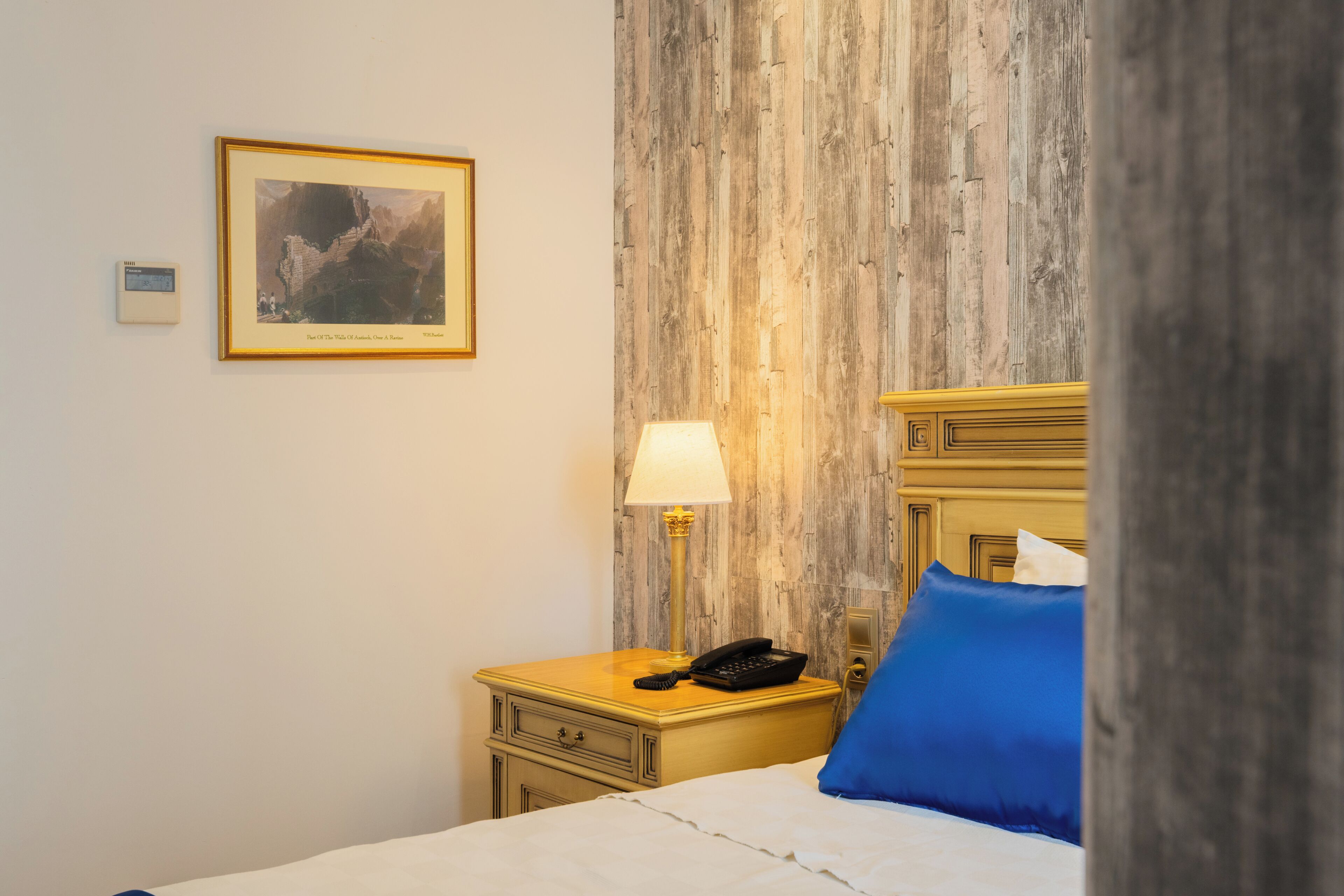 Habitación de hotel con cama, mesita de noche con lámpara, cuadro en la pared y pared decorativa de madera.