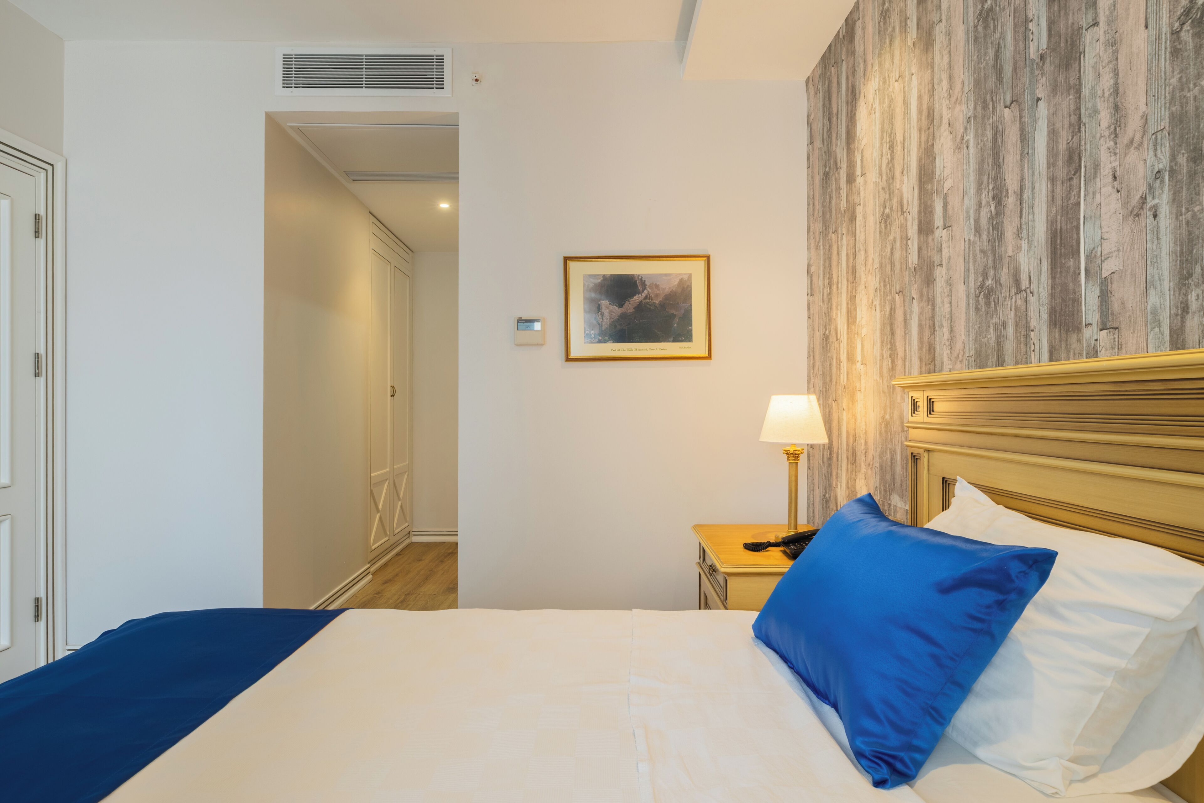 Une chambre d’hôtel avec un lit, une table de chevet avec une lampe, un tableau encadré au mur et un mur d’accent en bois.