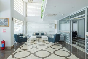 Un vestíbulo moderno con techo alto, un extintor, una zona de estar con sofás y sillones, y un suelo con diseño.