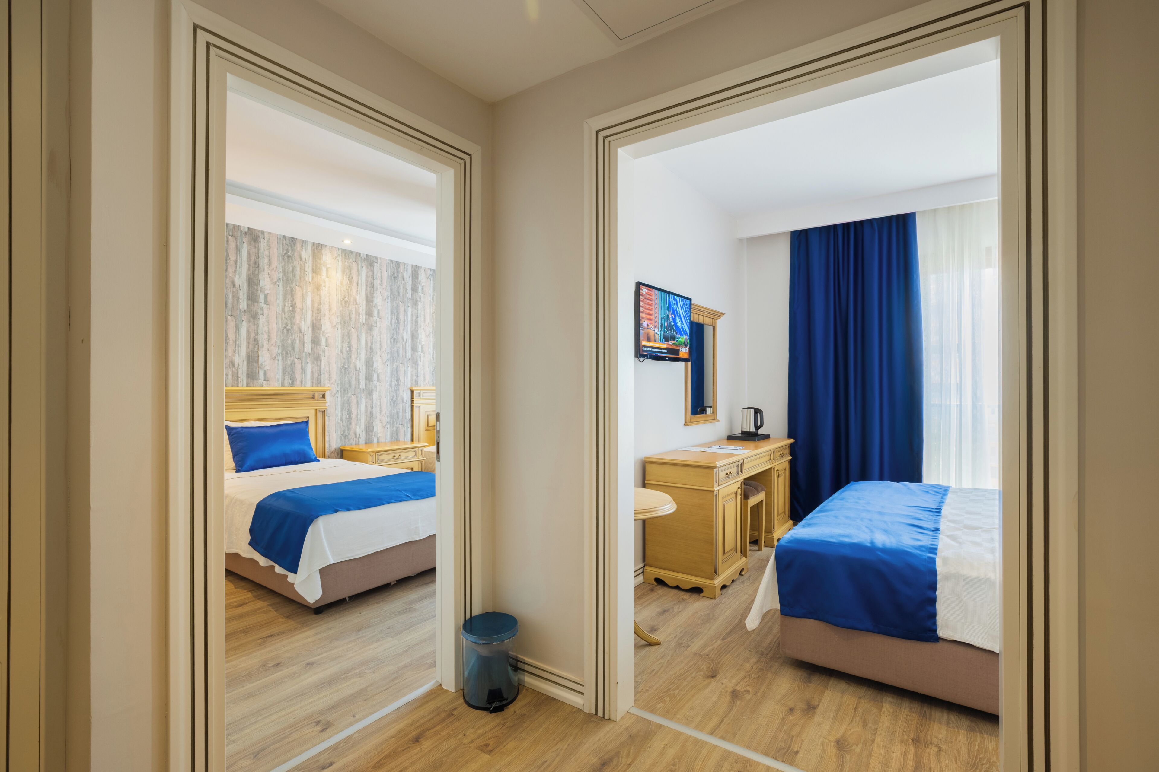 A hotel room with two beds, a desk, a TV, and a window with curtains.
