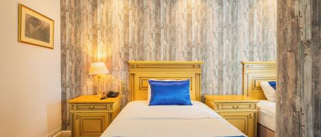 A hotel room with a wooden wall panel, a bed with blue bedding, two bedside tables, and a nightstand with a lamp.