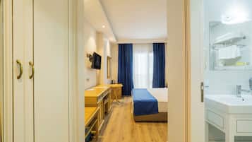 Hotellihuone, jossa on sänky, työpöytä, peili sekä kylpyhuone, jossa on pesuallas ja pyyheteline.