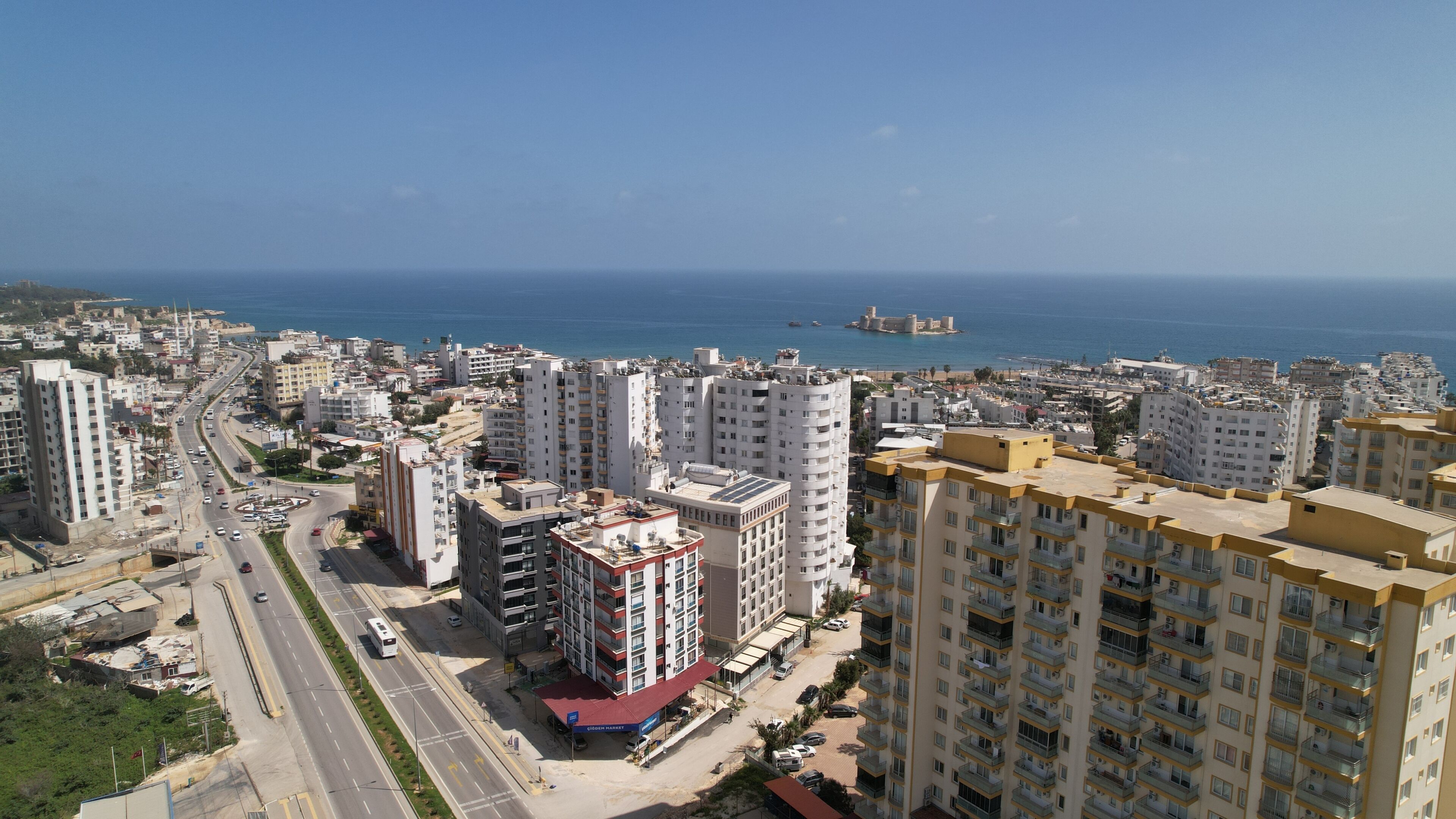 A coastal cityscape with high-rise buildings, a clear blue sky, and a view of the sea.