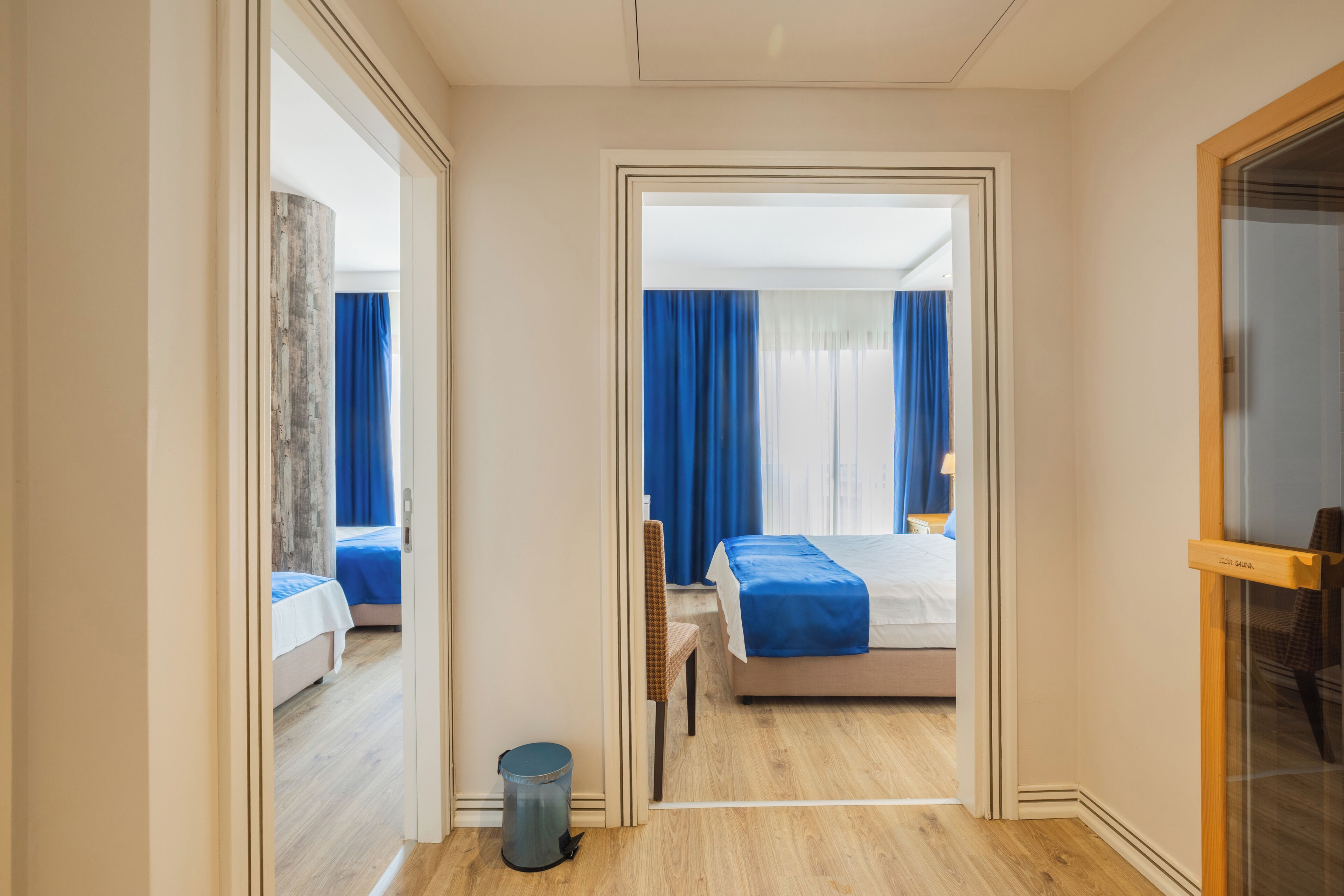 A hotel room with a bed, a chair, a small trash bin, and a mirror.