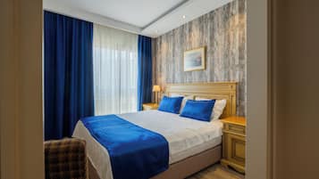 A hotel room with a large bed, a wooden headboard, a nightstand, a chair, and a window with curtains.
