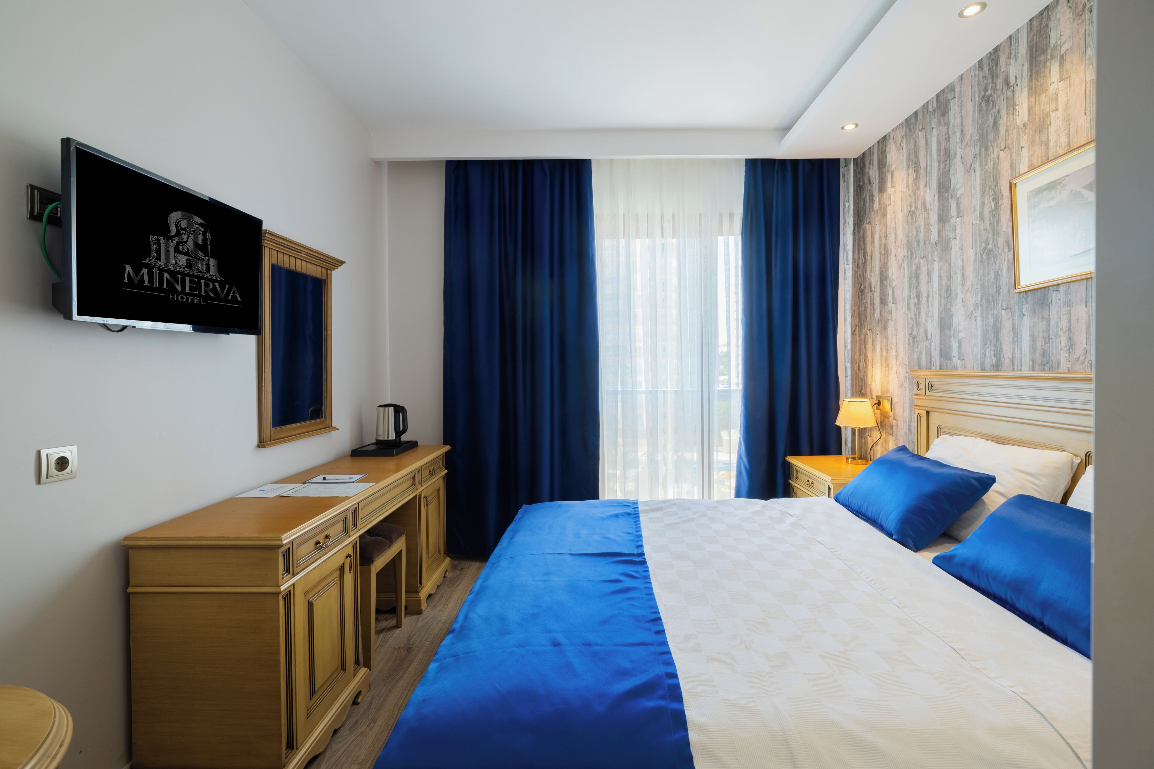 Habitación de hotel con cama, escritorio, televisor y ventana con cortinas.