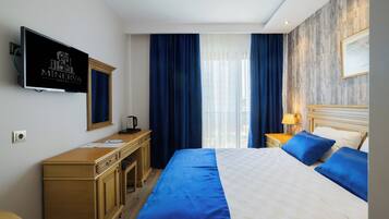 Habitación de hotel con cama, escritorio, televisor y ventana con cortinas.
