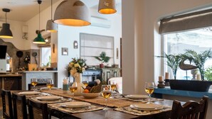 A dining table set with plates, glasses, and a bowl of fruit, with hanging pendant lights above. - Staymaster Villa Anasoh 4BHK (Vagator)