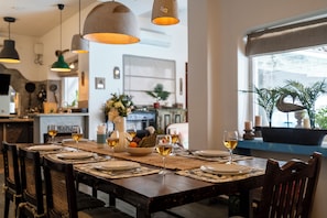 A dining table set with plates, glasses, and a bowl of fruit, with hanging pendant lights above. - Staymaster Villa Anasoh 4BHK (Vagator)
