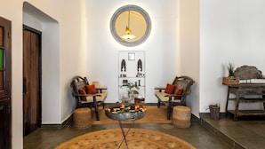 A lobby with a round wooden table, two armchairs, a mirror, and a wall-mounted shelf with decorative items. - Staymaster Villa Anasoh 4BHK (Vagator)