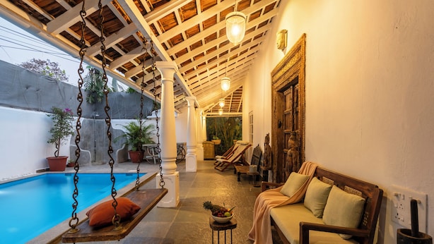 A pool area with a swing chair, a wooden bench, and a sofa with cushions. - Staymaster Villa Anasoh 4BHK (Vagator)