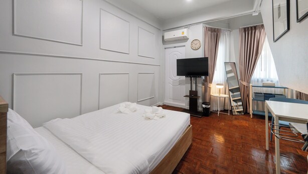 A hotel room with a bed, a desk, a TV, and a window with curtains. - Arun Sa Wad House Sukhumvit 2 Guests (Bangkok)