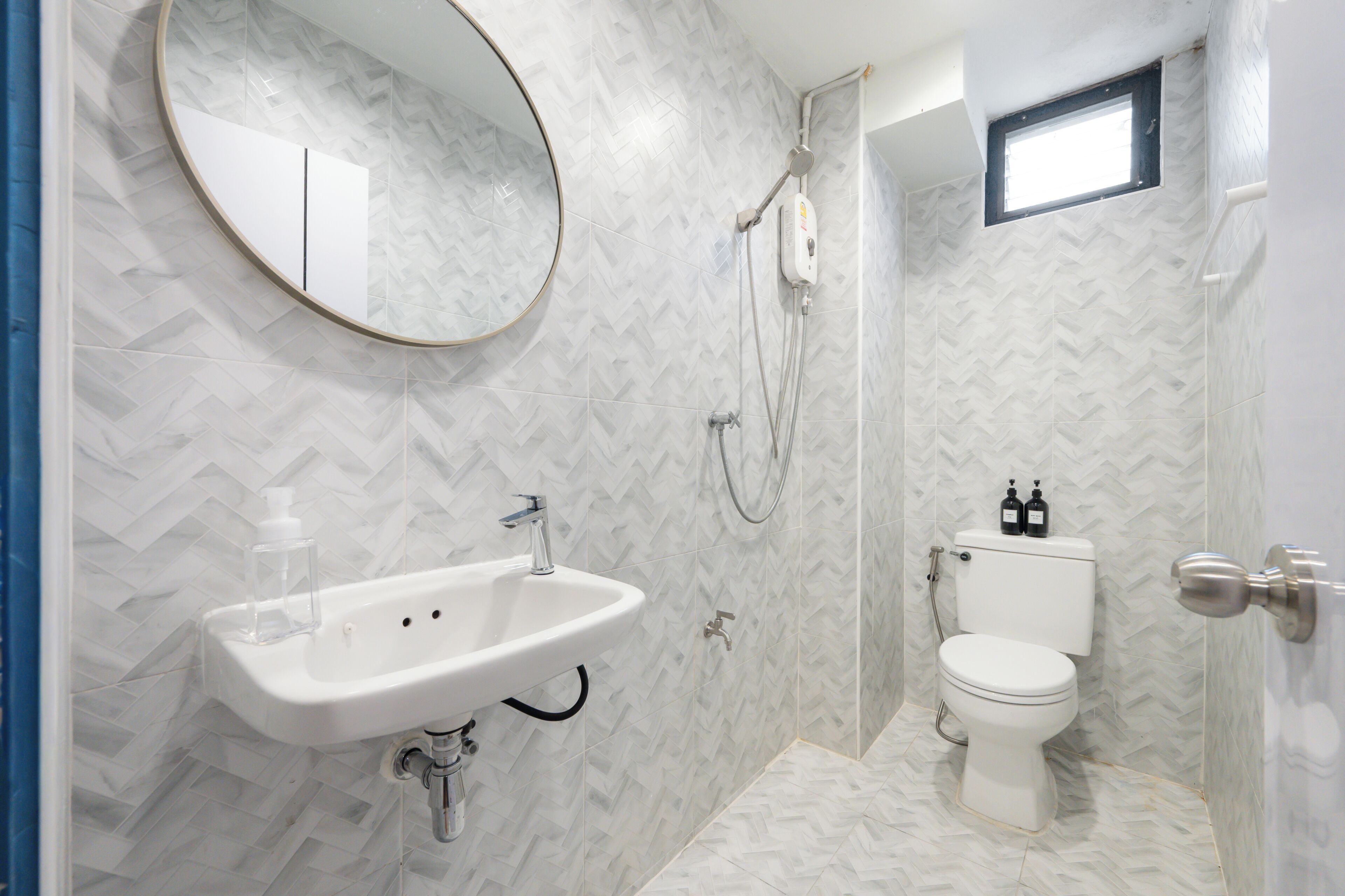 Une salle de bain avec un carrelage disposé en motif de chevron, un lavabo blanc, des toilettes et une douche.