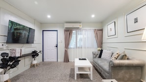 A living room with a sofa, a coffee table, a TV, and a door. - Arun Sa Wad House Sukhumvit 2 Guests (Bangkok)