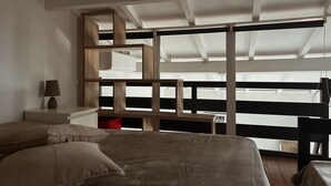 Un dormitorio con cama, mesita de noche, lámpara, estante de madera y vistas a través de amplias ventanas.