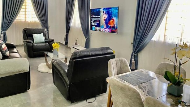 Una sala de estar moderna con un sofá, una silla, una mesita de centro y un televisor montado en la pared.