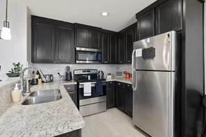 A modern kitchen with dark cabinets, stainless steel appliances, and a granite countertop. - Furnished 2BR/2BA Monthly • Comfy King • Workspace + Laundry • Near Hospitals (Edinburg)