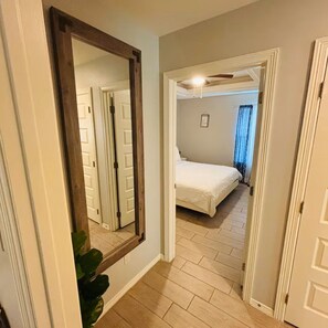 A hallway leading to a bedroom with a bed, a large mirror, and a ceiling fan. - Furnished 2BR/2BA Monthly • Comfy King • Workspace + Laundry • Near Hospitals (Edinburg)