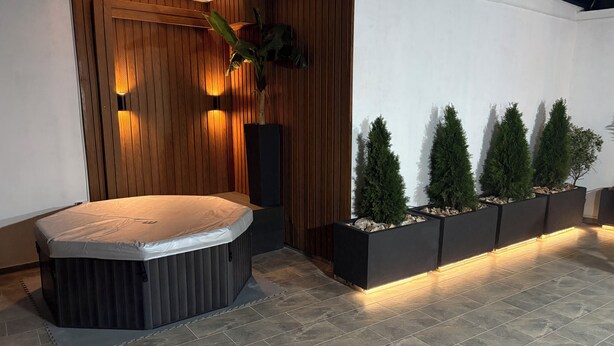 A modern spa area with a hot tub, wooden panel walls, and a row of planters with coniferous trees. - GoldApartment  (Sarandë)