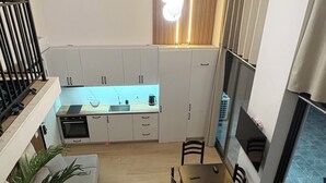 A modern kitchen with white cabinets, a dining area with a table and chairs, and a staircase leading to an upper level. - GoldApartment  (Sarandë)