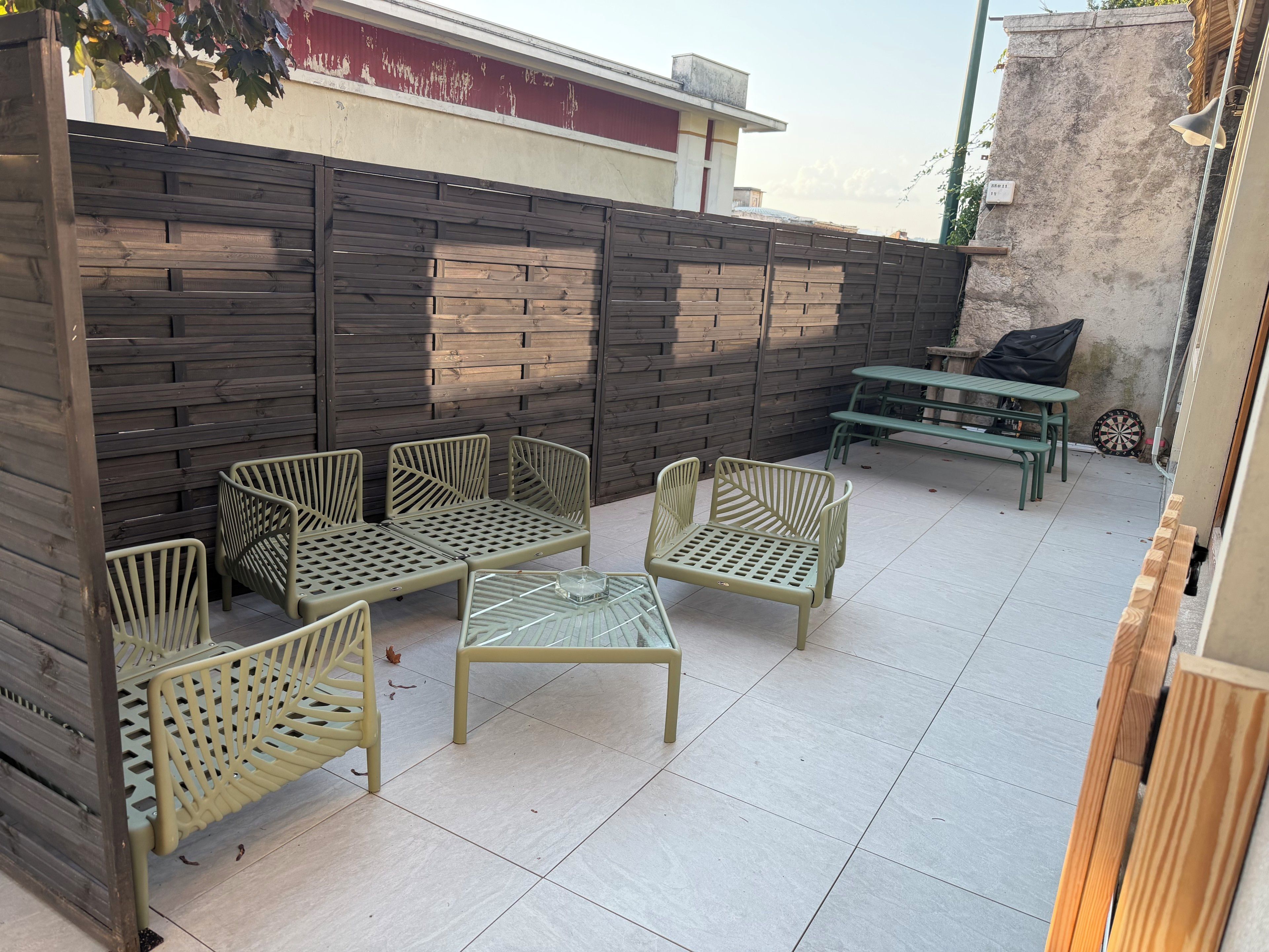 Une terrasse extérieure avec des meubles en métal, une clôture en bois et une table sur laquelle est posé un jeu de fléchettes.