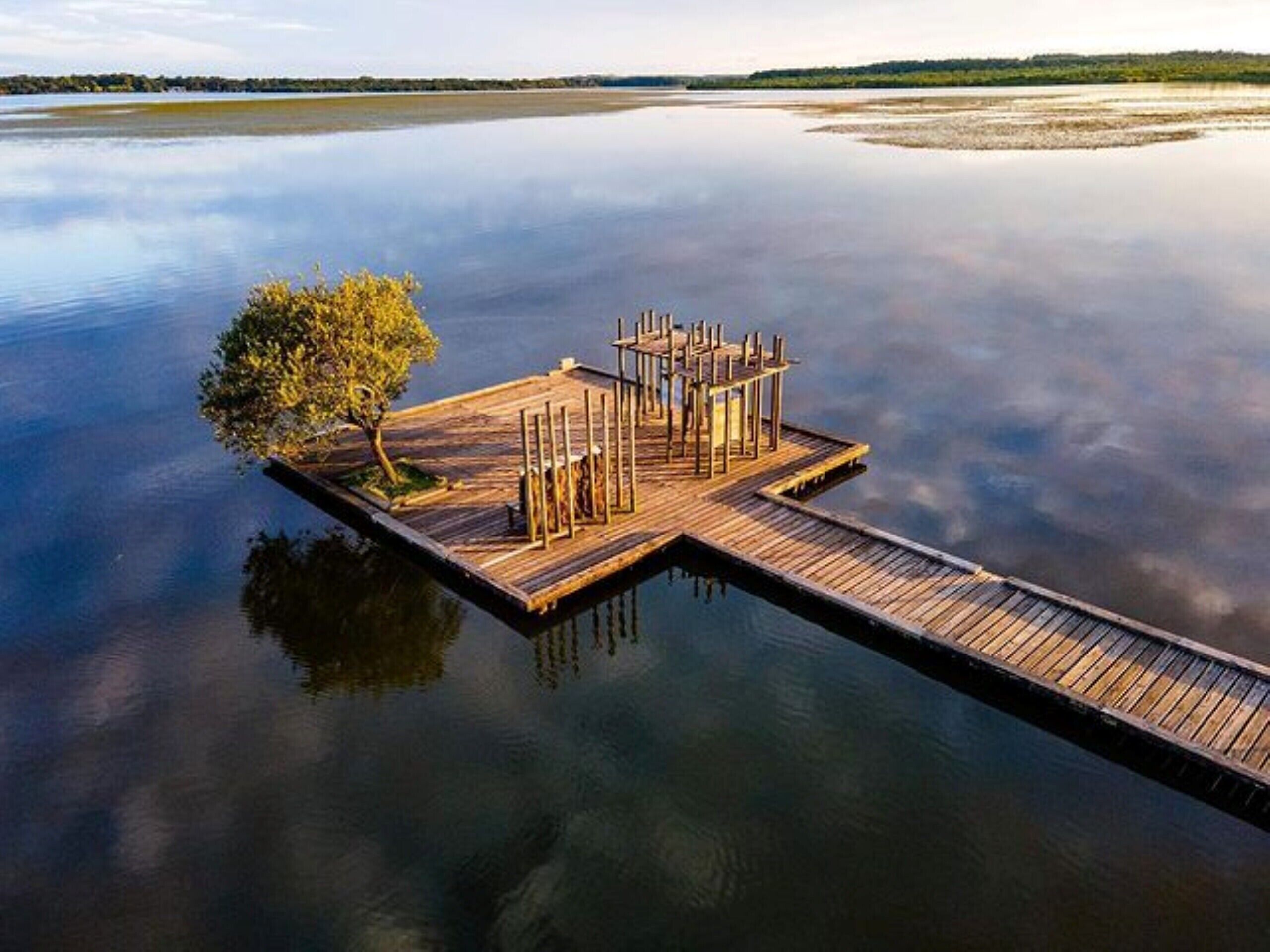 A wooden dock extending into calm water, surrounded by a natural landscape.